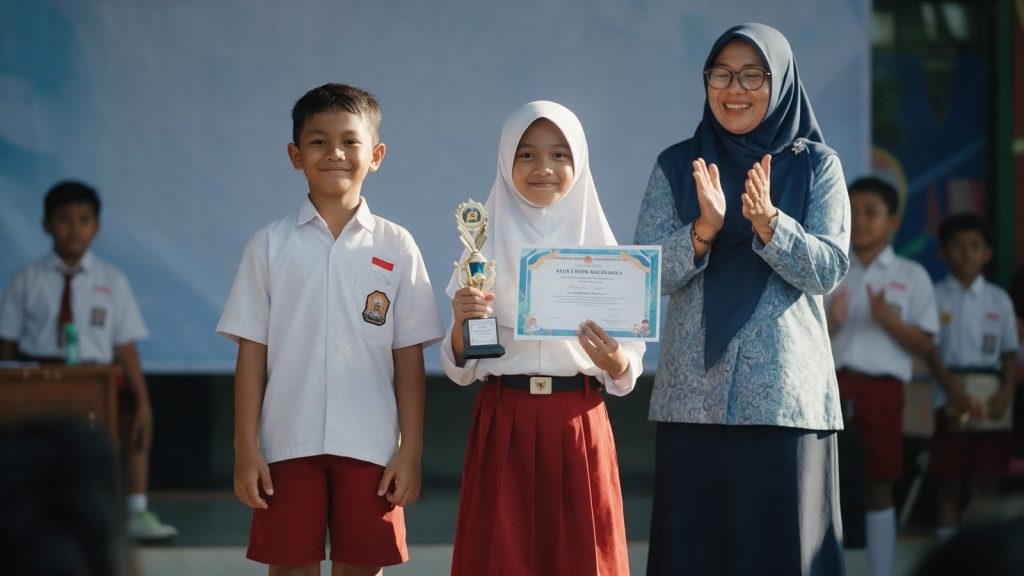 Dua murid SD membawa piala dan piagam lomba matematika